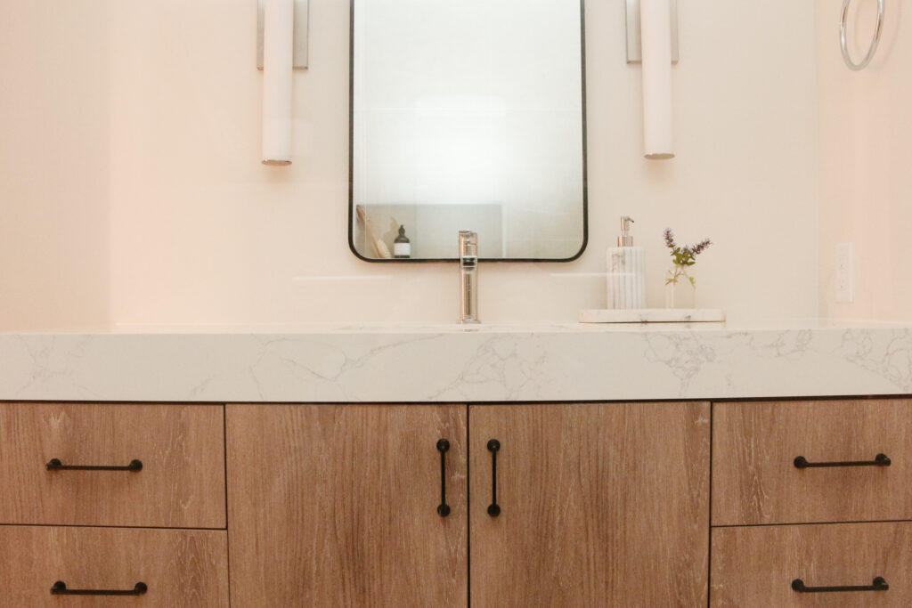 A MCM vanity in a warm basement bathroom with thick quartz top, black hardware