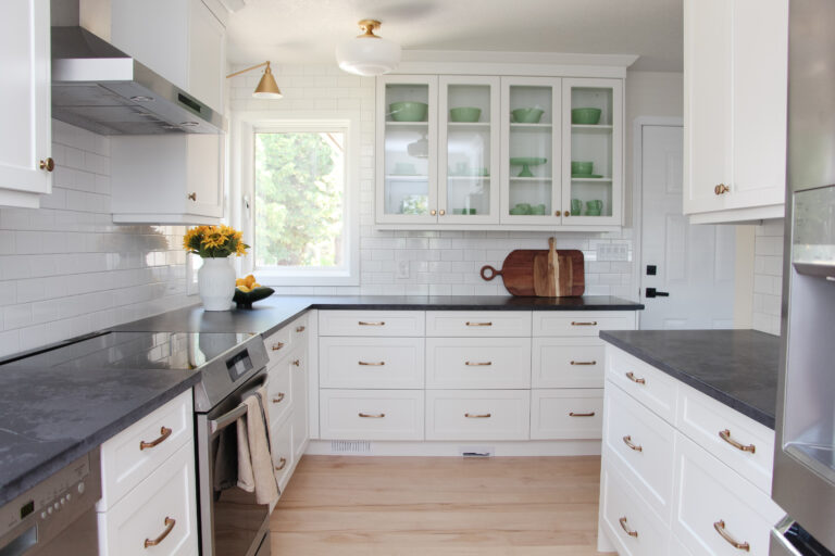 timeless white kitchen cabinets, black quartz counter, gold sconce over window, sunflowers and lemon decor, subway tile to ceiling, glass cabinets, jadeite collection