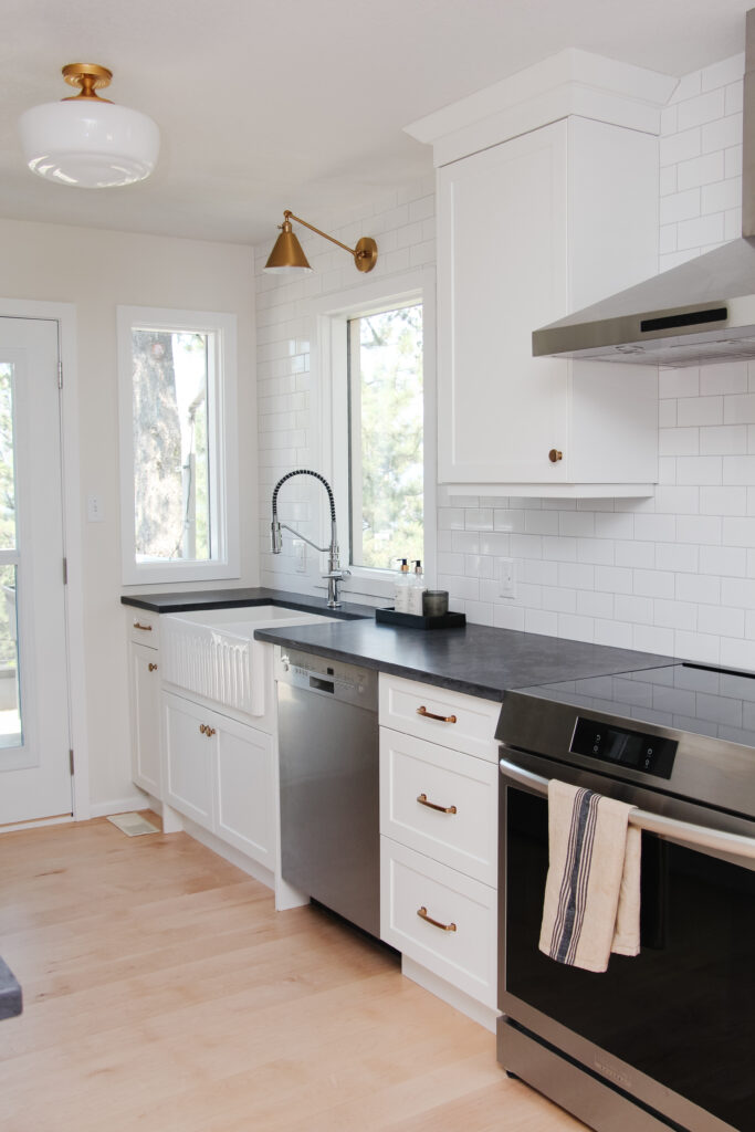 white galley kitchen with black quartz countertop, farmhouse sink, gold hardware