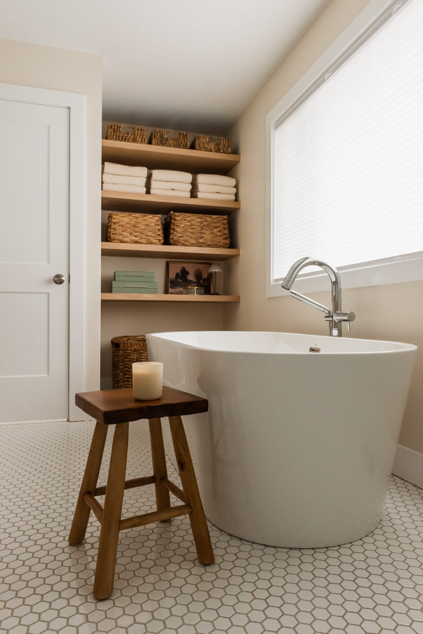 transitional primary ensuite, warm wood tones and white tile, stand alone tub under window