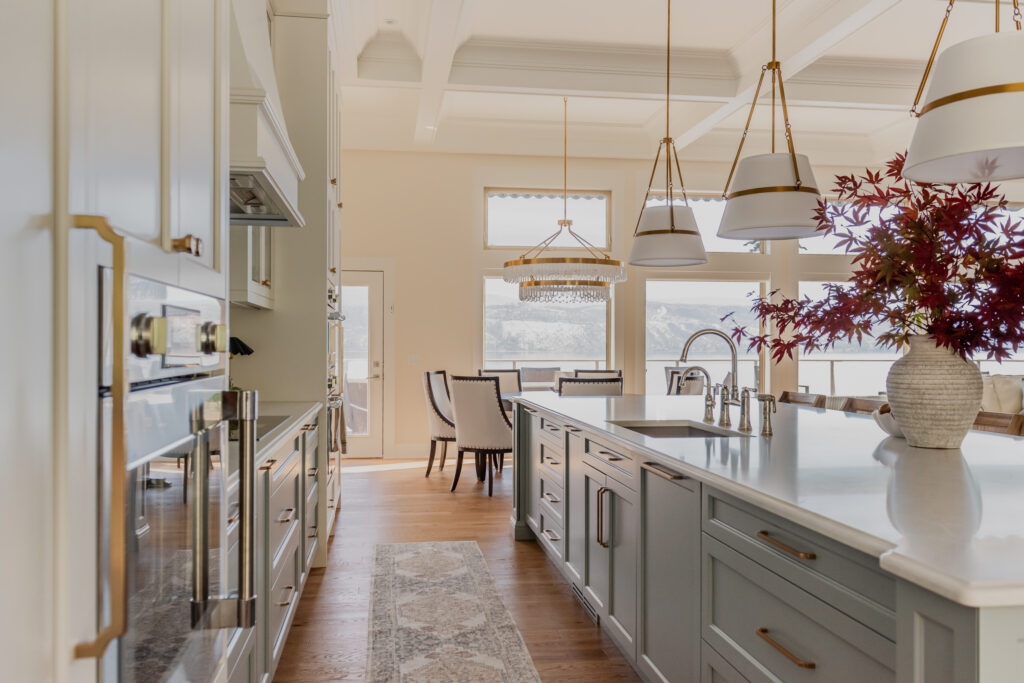 Light blue kitchen island with coffered ceiling and ogee countertop edge in a bright, transitional kitchen with tiered chandelier