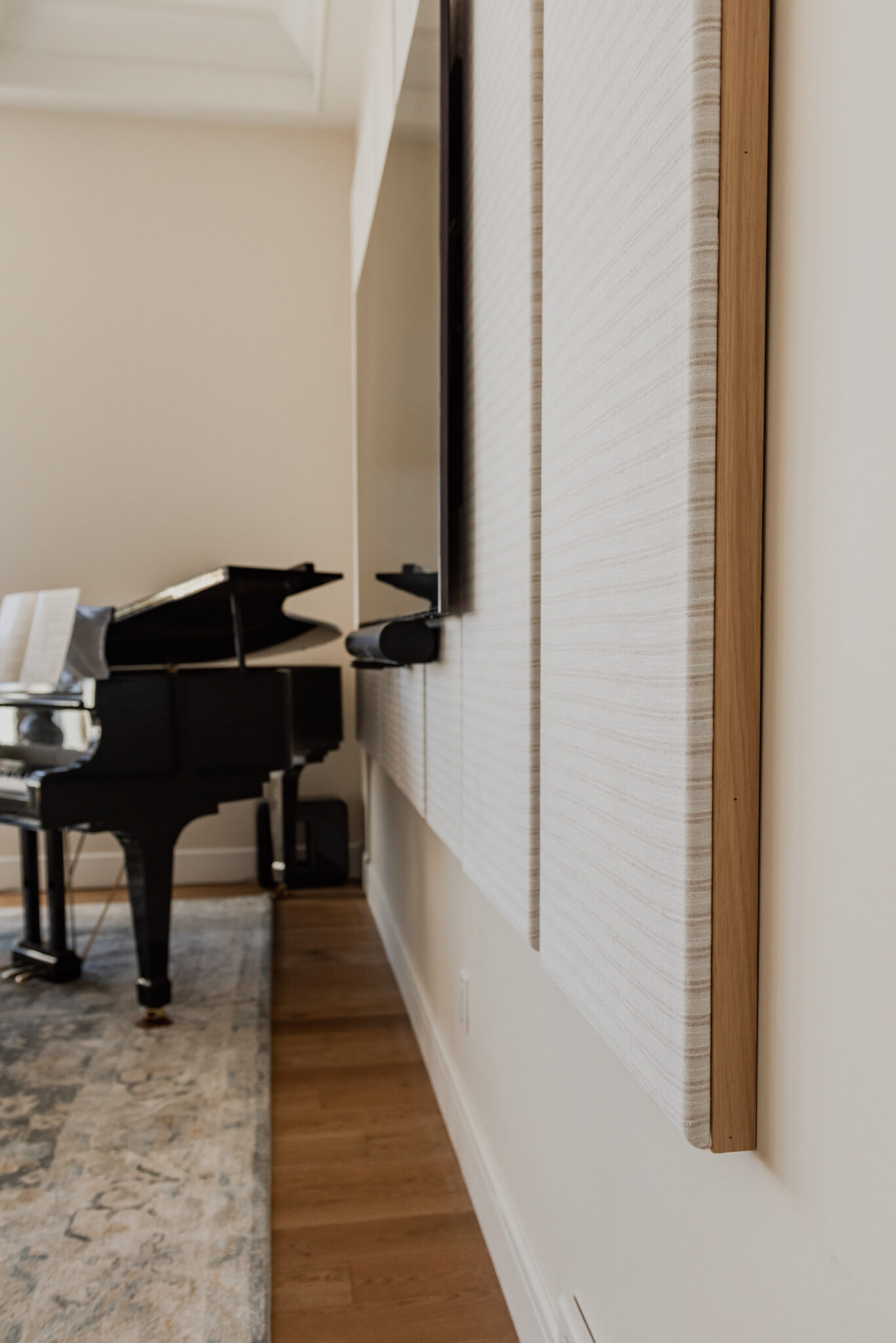 Custom fabric-wrapped acoustic wall panels framed in natural oak, installed behind a television for subtle sound absorption.