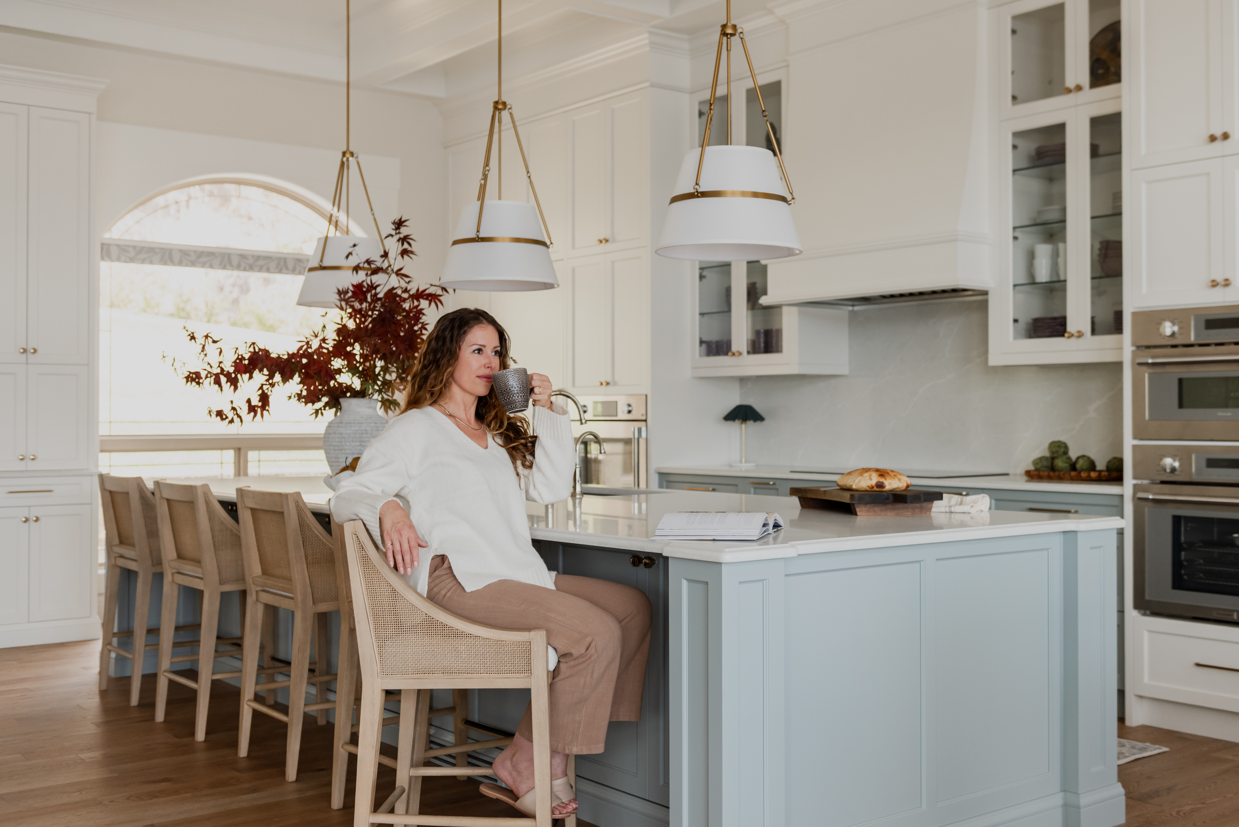 Woman in Custom 6-foot range hood feature wall with integrated Thermador appliances, coffered ceilings, and a spacious entertaining island.