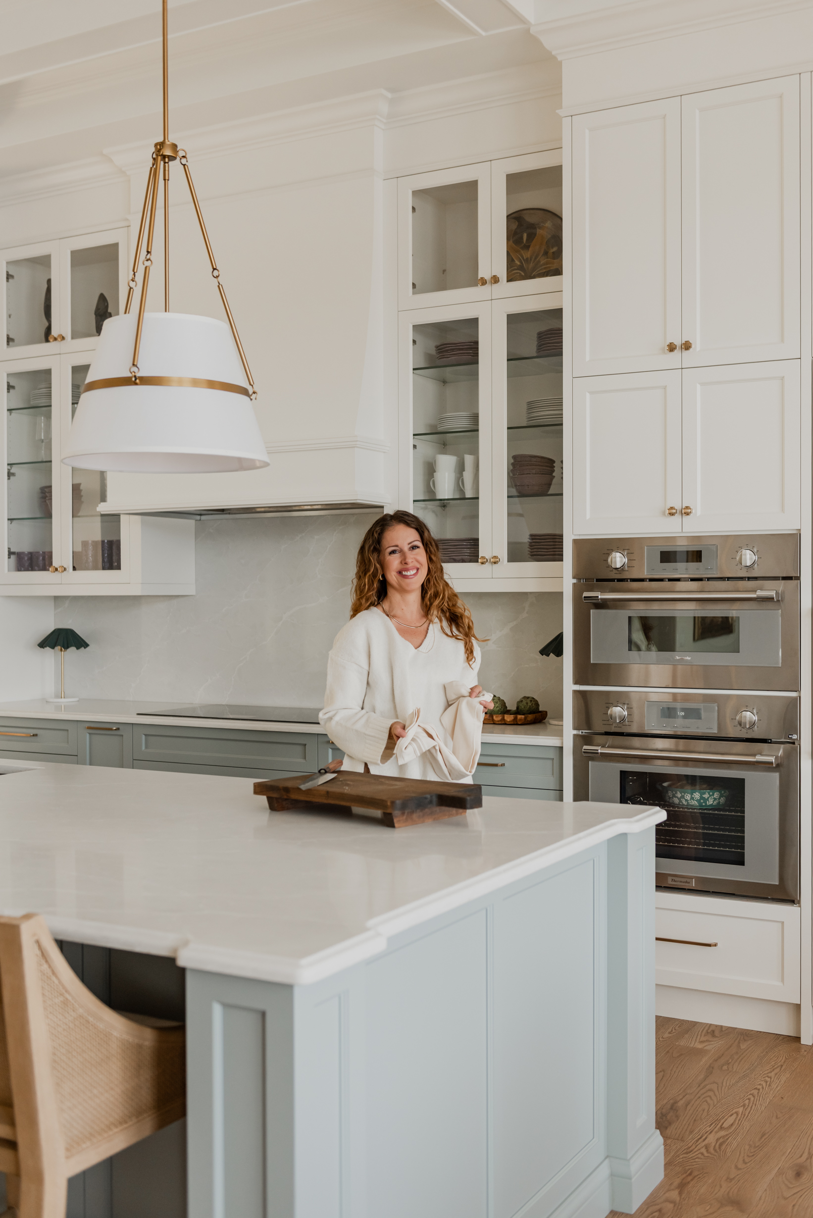 Woman in Custom 6-foot range hood feature wall with integrated Thermador appliances, coffered ceilings, and a spacious entertaining island.