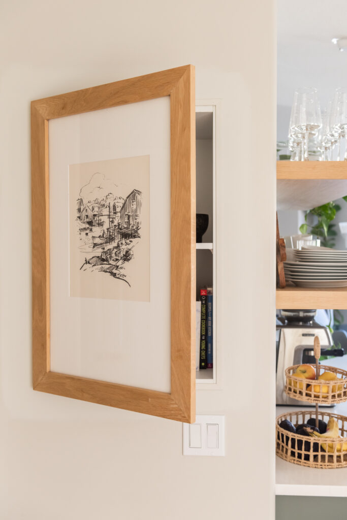Kitchen wall detail showing flush framed art panel that opens to reveal concealed storage behind.