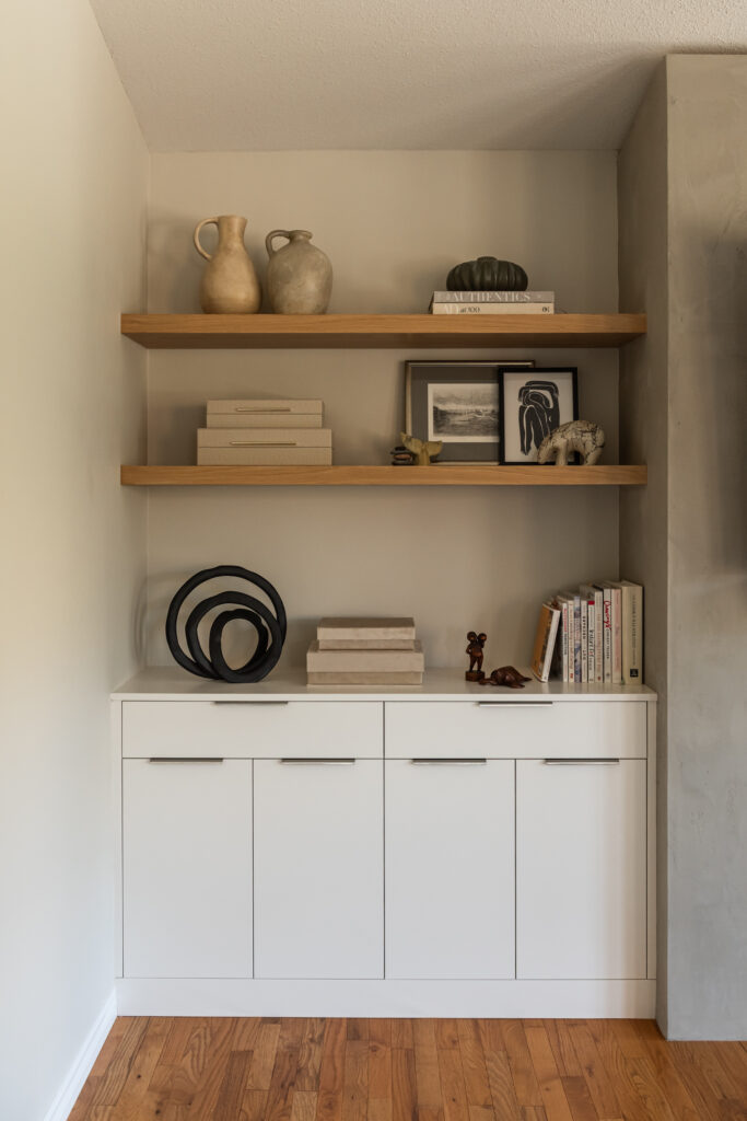 Custom living room built ins with closed cabinetry for storage and white oak open shelving styled with art and decor.
