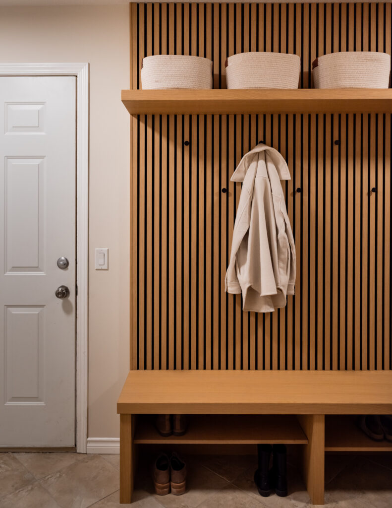Scandinavian inspired mud hall with wood slat wall, custom bench seating, integrated shoe storage, and wall hooks for everyday family use.