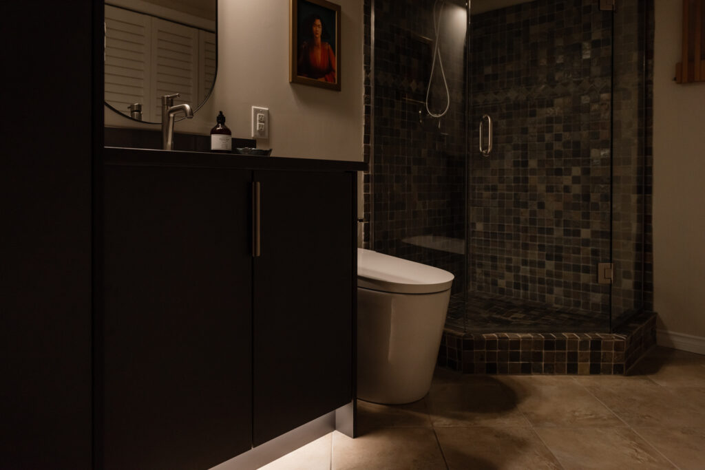 Basement bathroom vanity with dark cabinetry, integrated toe kick lighting, and modern faucet for a budget friendly refresh.