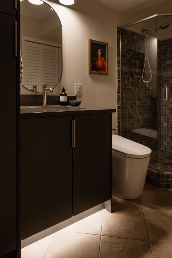 Basement bathroom vanity with dark cabinetry, integrated toe kick lighting, and modern faucet for a budget friendly refresh.