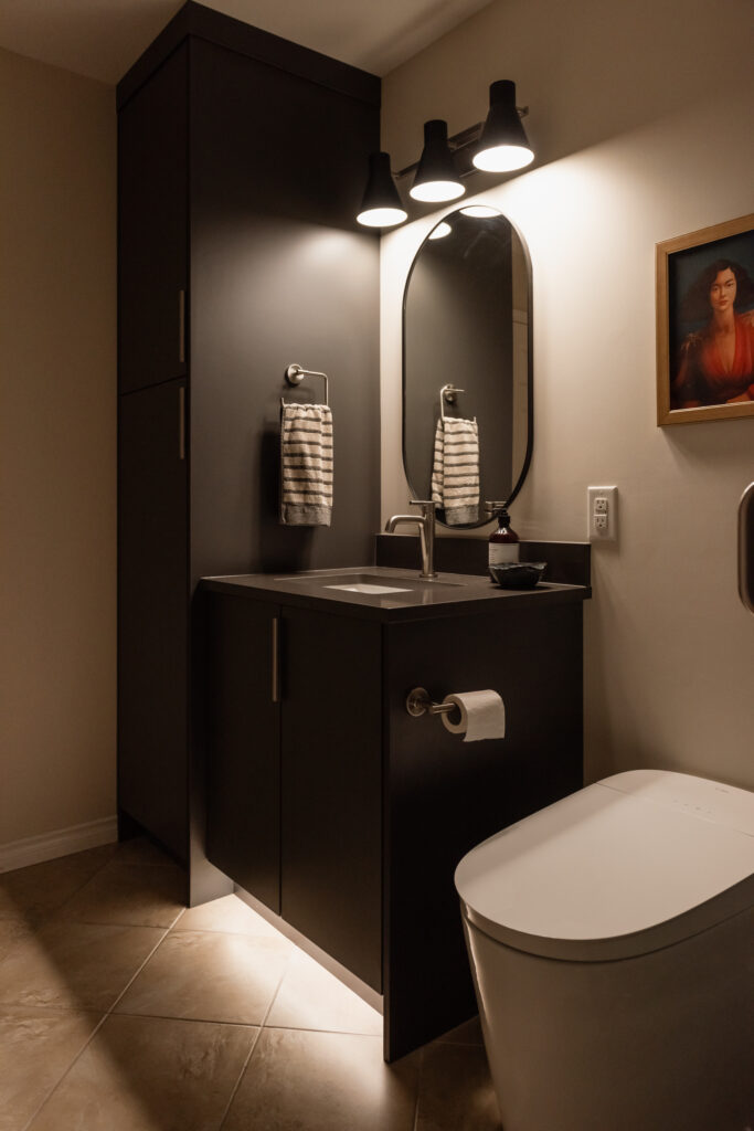 Basement bathroom vanity with dark cabinetry, integrated toe kick lighting, and modern faucet for a budget friendly refresh.