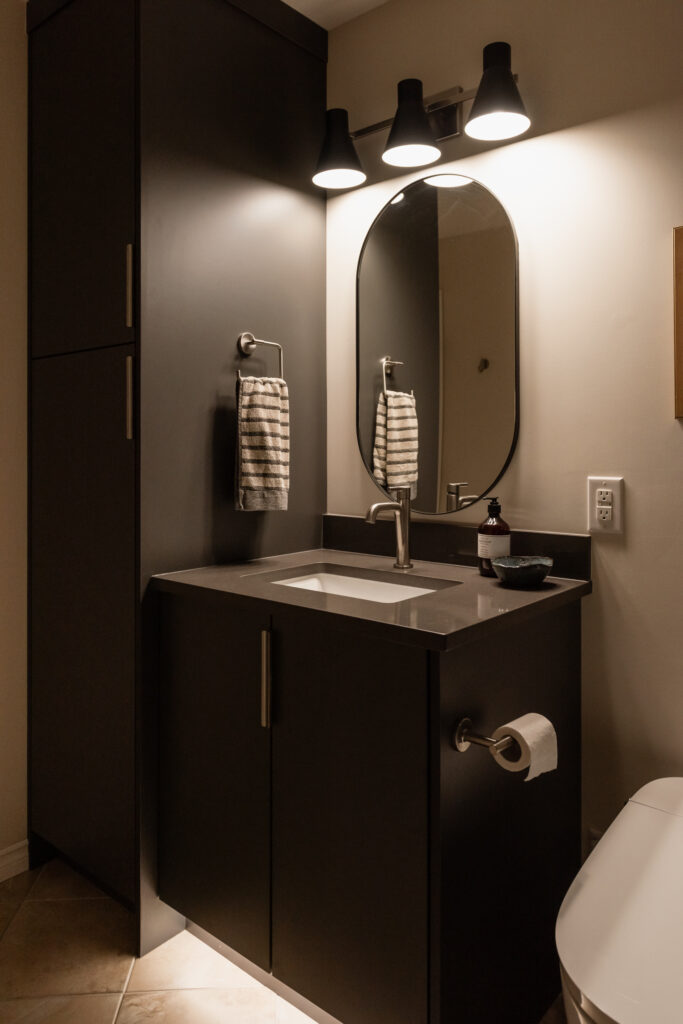 Basement bathroom vanity with dark cabinetry, integrated toe kick lighting, and modern faucet for a budget friendly refresh.