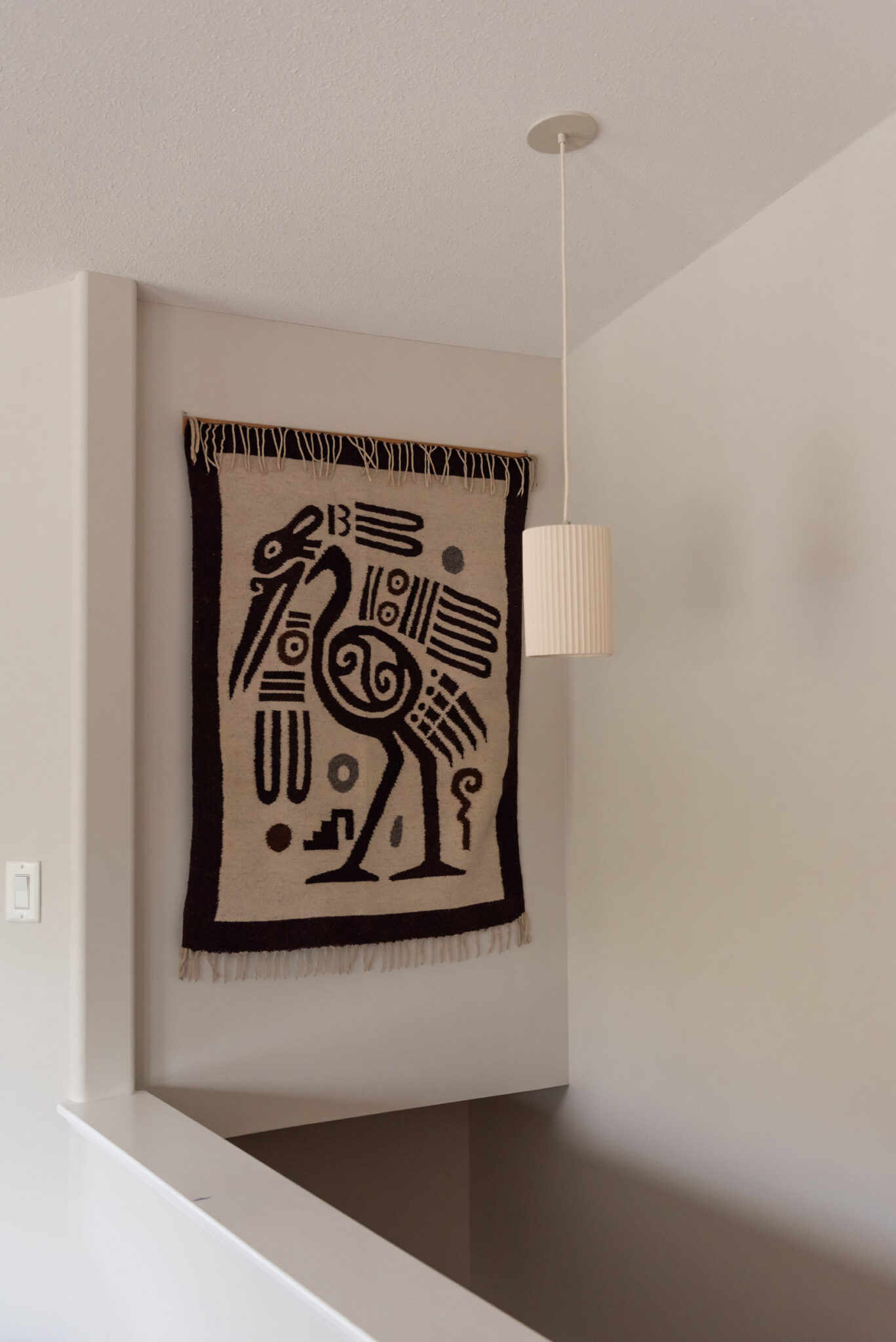 Stairwell wall with filled in niche and woven tapestry, replacing a dated recessed niche for a cleaner architectural look.