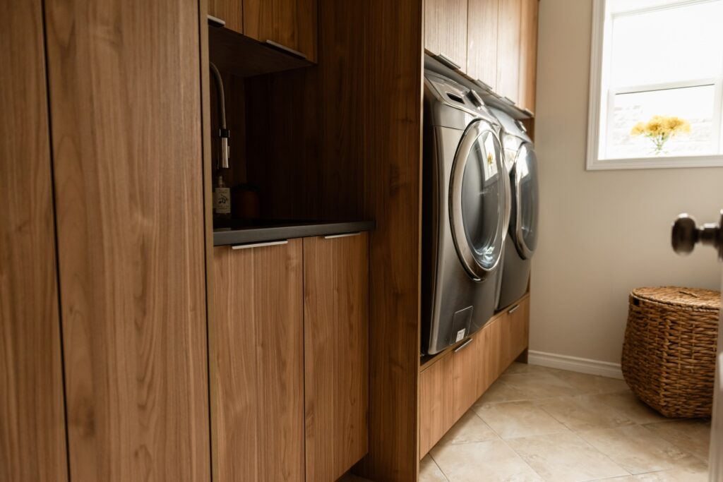 Custom laundry room cabinetry with integrated sink, upper cabinets, and warm wood grain finish for a cohesive, elevated look.
