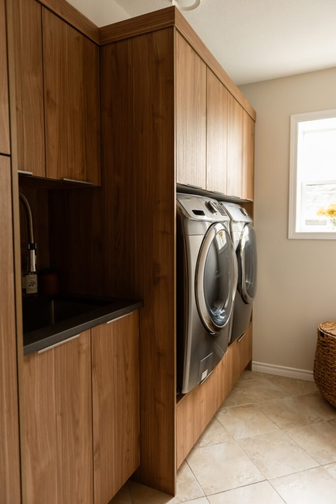 Custom laundry room cabinetry with integrated sink, upper cabinets, and warm wood grain finish for a cohesive, elevated look.
