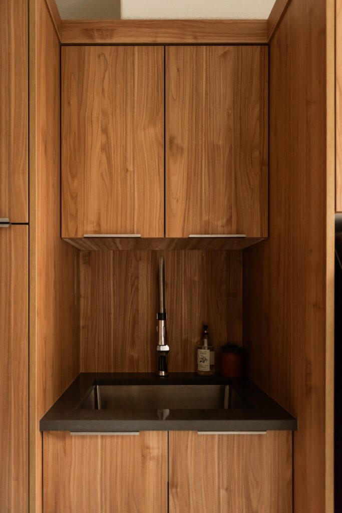 Custom laundry room cabinetry with integrated sink, upper cabinets, and warm wood grain finish for a cohesive, elevated look.