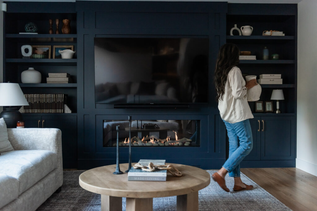 Woman decorating built in cabinetry in modern living room with linear fireplace