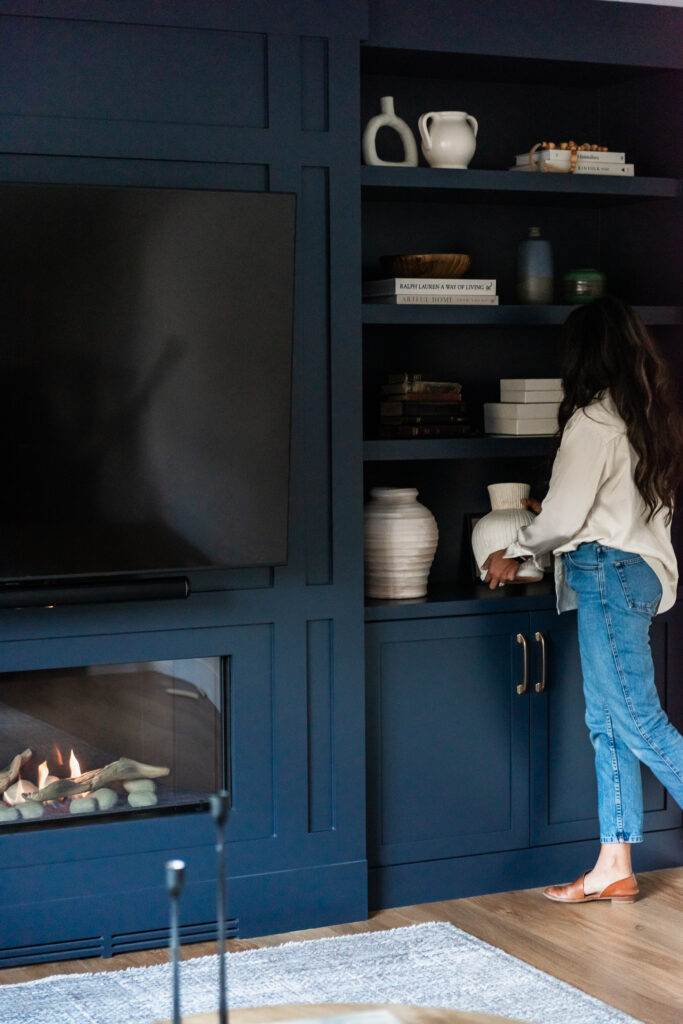 Woman decorating built in cabinetry in modern living room with linear fireplace