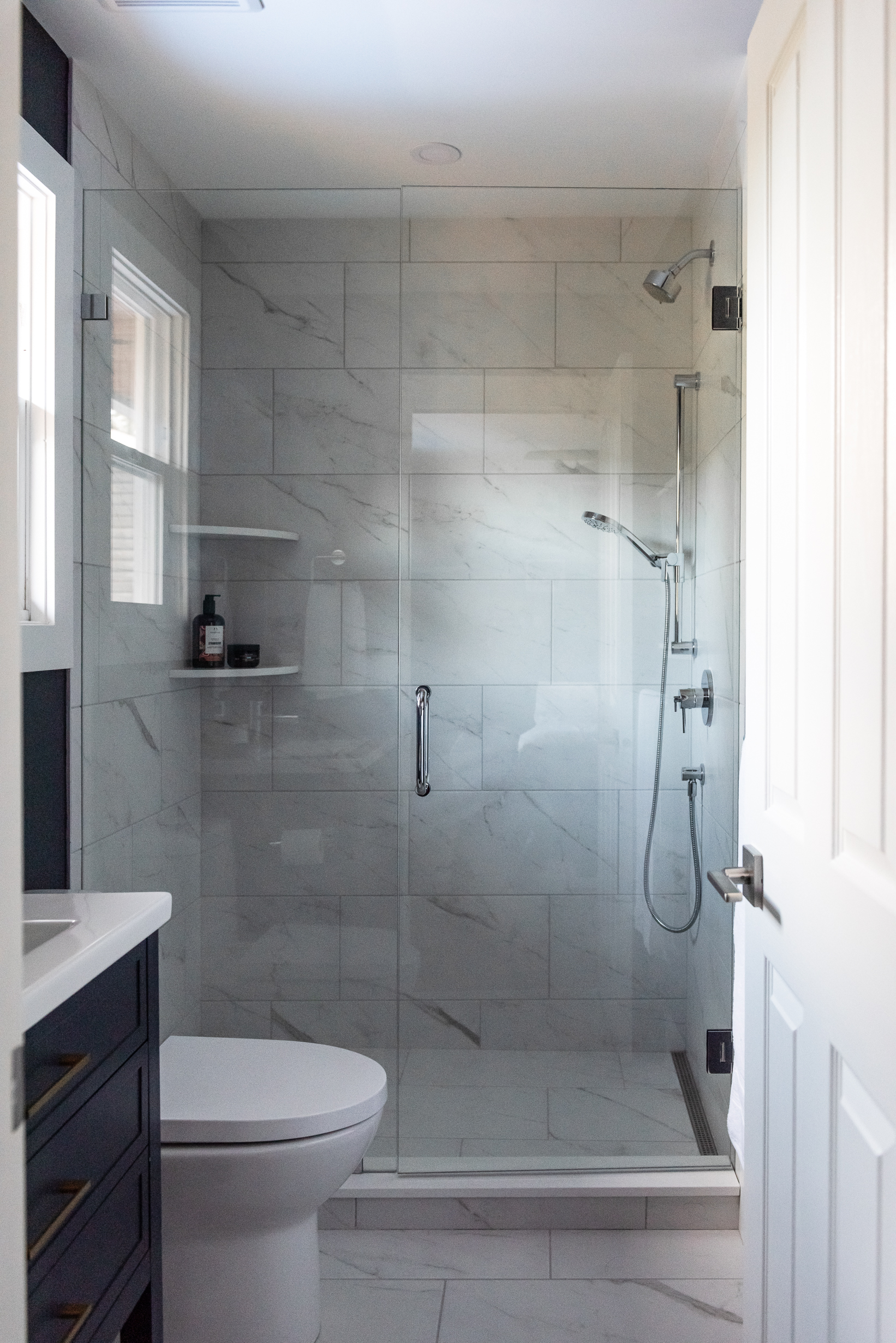 Small ensuite with colour drenched navy vanity and marble look tiled shower