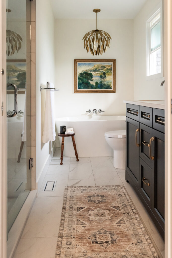 Renovated primary ensuite with deep hunter green vanity, freestanding tub, and brass lighting