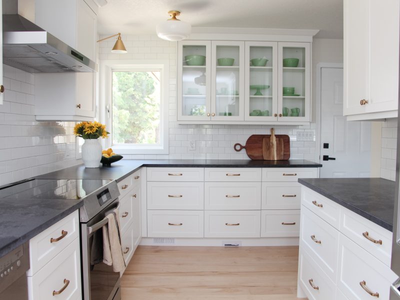 timeless white kitchen cabinets, black quartz counter, gold sconce over window, sunflowers and lemon decor, subway tile to ceiling, glass cabinets, jadeite collection