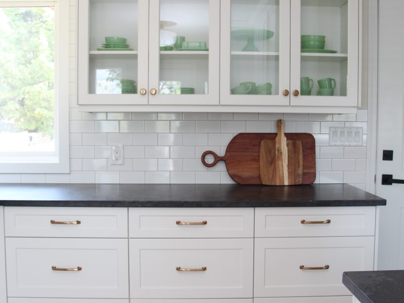 timeless white kitchen cabinets, black quartz counter, gold sconce over window, sunflowers and lemon decor, subway tile to ceiling, glass cabinets, jadeite collection