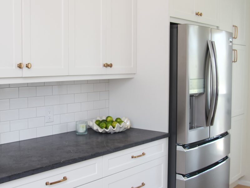 white galley kitchen with black quartz countertop, bowl of limes, gold hardware